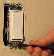 Man's fingers screwing a light switch into a mounting slot.
