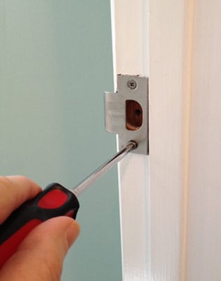 A hand using a screwdriver to adjust the position of the strike plate. 