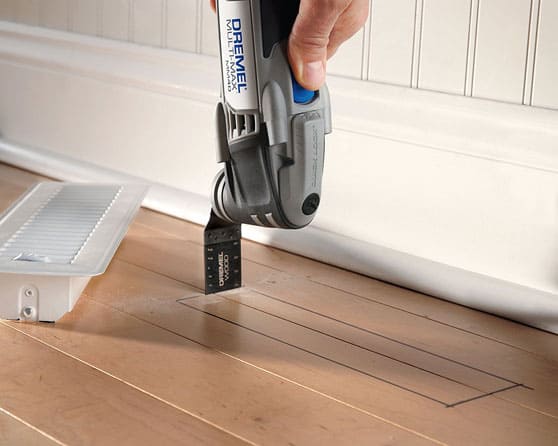 An oscillating multi-tool, plunge cutting a wooden floor for a heating vent.