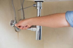 Man turning off water to sinks and toilets at the small valve beneath them. 