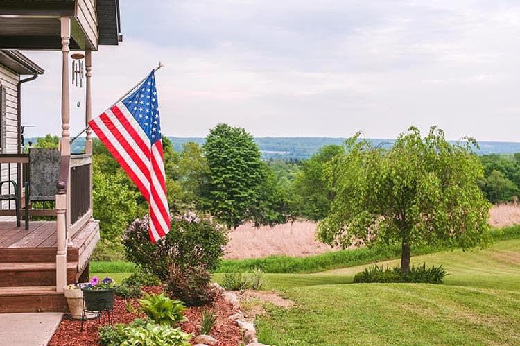 An American flag hung on a house's porch including a front yard.
