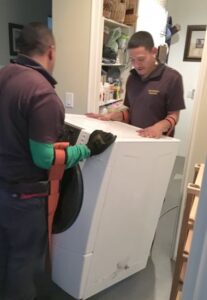 Two men carrying a washing machine using heavy-duty arm straps.